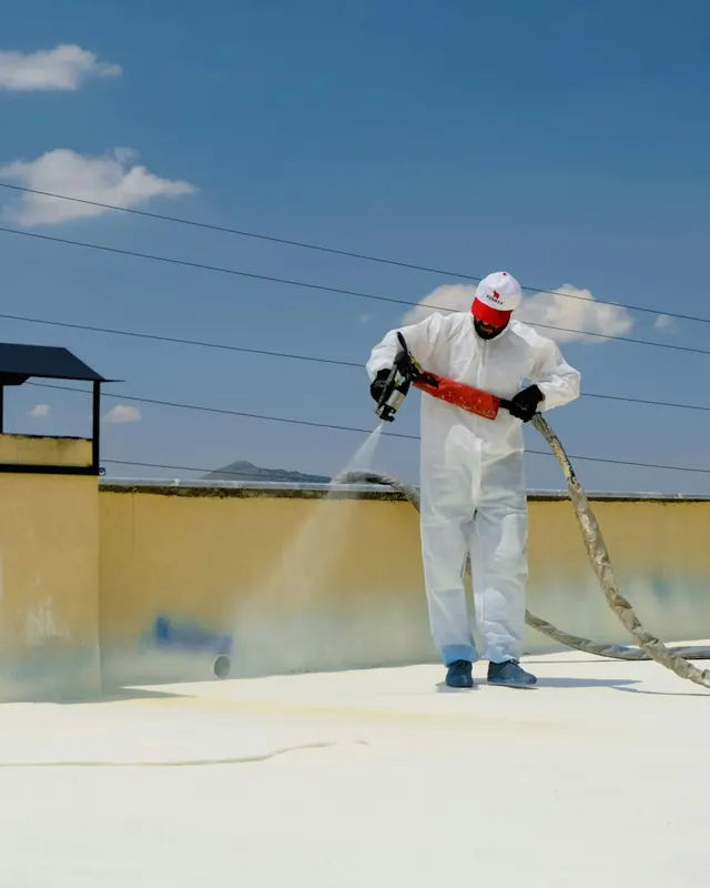 A worker in protective overalls spraying a waterproof coating across a roof