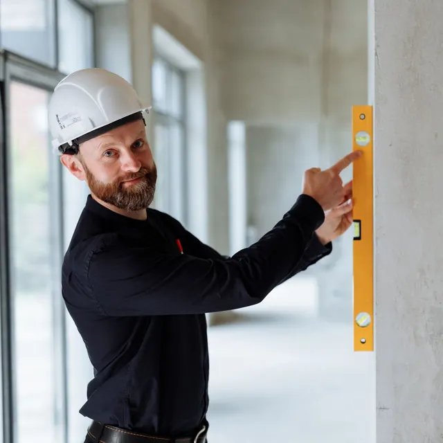 A site engineer in a hard hat checking a wall with a spirit level