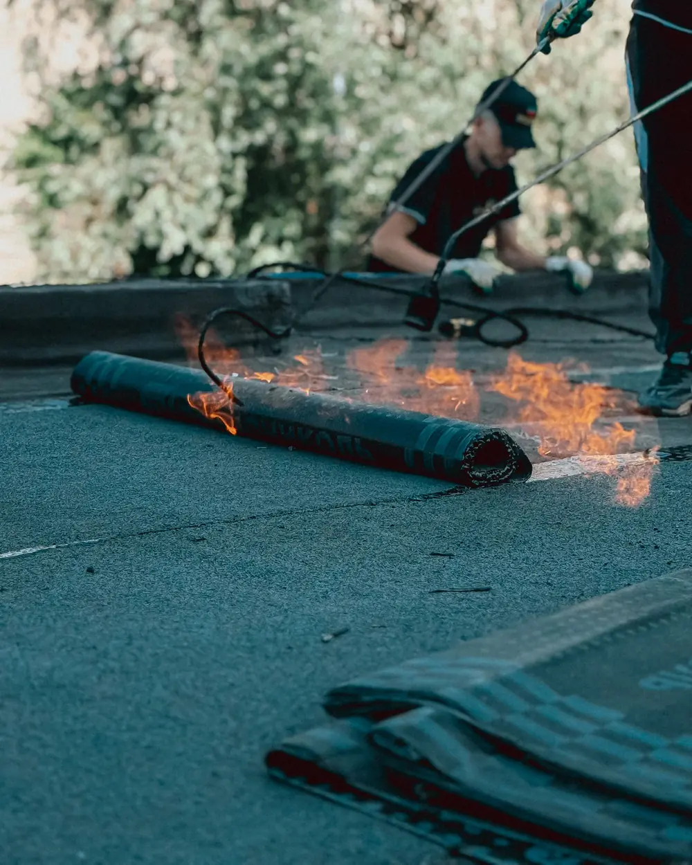 A roll of waterproofing membrane being heat-bonded with a gas torch on a flat roof