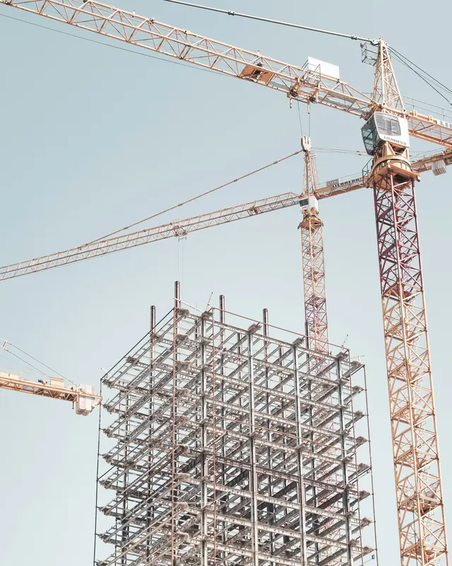 A steel-framed multi-storey building rising beside two tower cranes