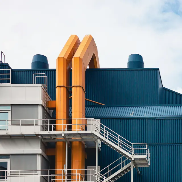 An industrial plant building clad in blue metal with orange ducting and access stairs