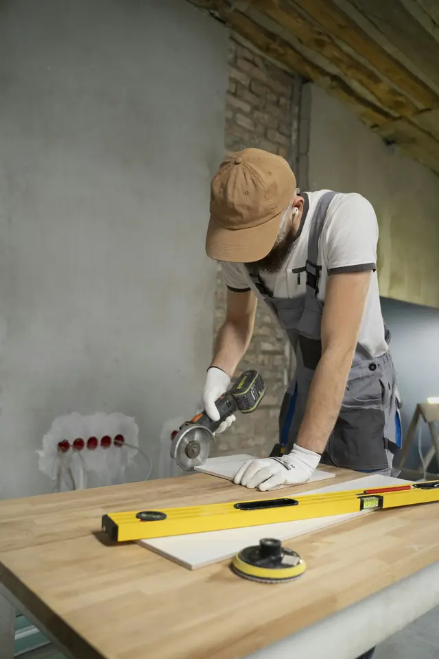 A tradesman in overalls cutting a board with an angle grinder during an interior refurbishment