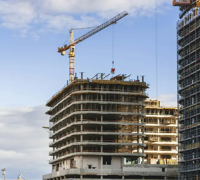 A multi-storey concrete residential building under construction with a tower crane