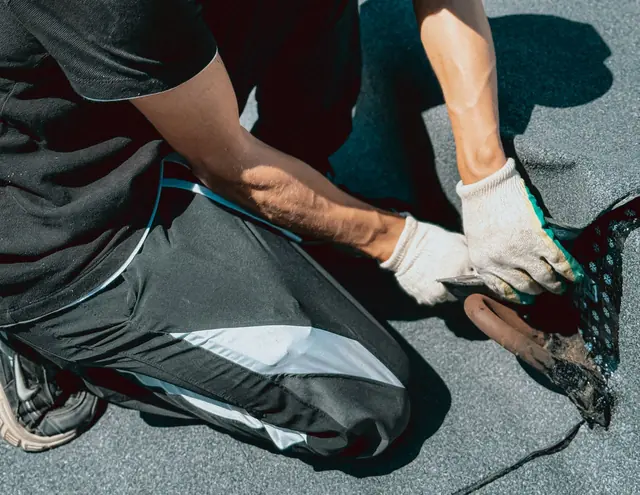 Gloved hands positioning the edge of a waterproofing membrane on a roof